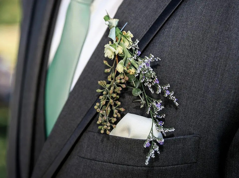 A man in suit and tie with flowers on his lapel.