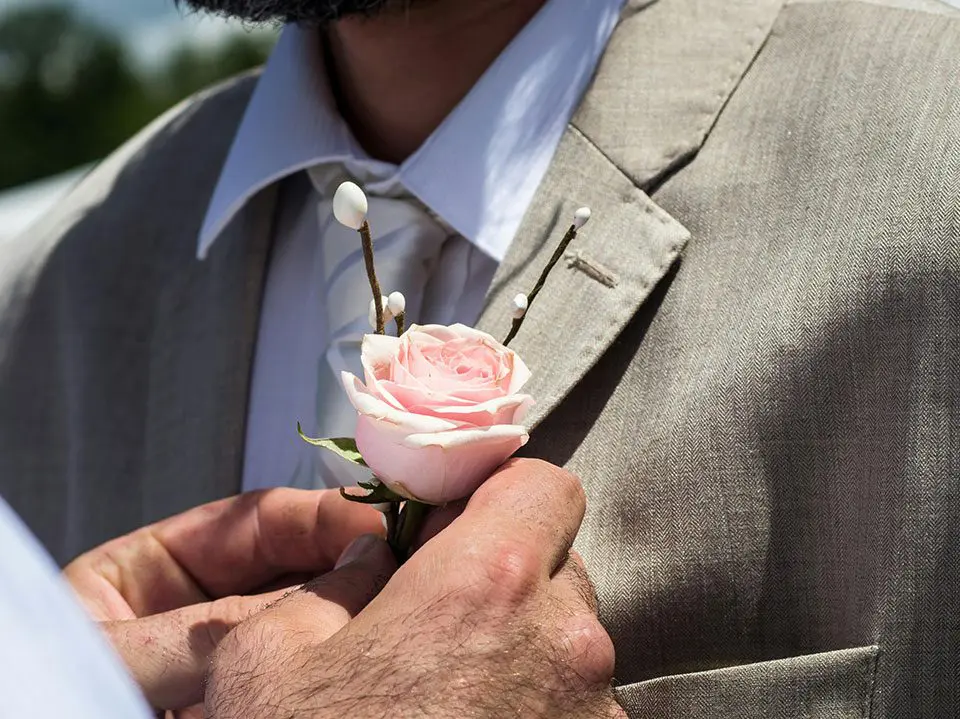 A man in suit and tie holding onto a flower.