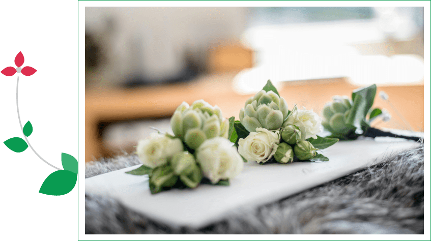 Two white flowers on a table with other things in the background.